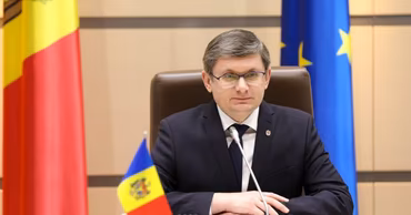 Igor Grosu sitting at a table with Moldovan and EU flags in the background.