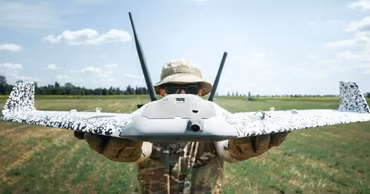 A soldier holding a military surveillance drone in a field.