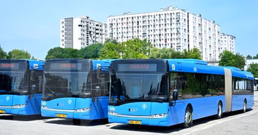 Several blue public transport buses parked in a lot in Chisinau with apartment buildings in the background.