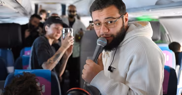 Navai holding a microphone inside an airplane cabin.