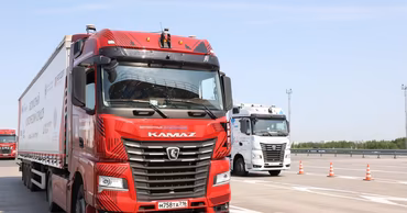 Two red and white Kamaz trucks driving on a highway.