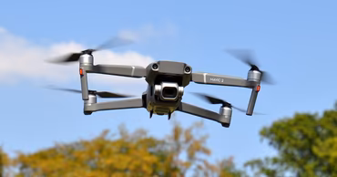 A professional DJI Mavic 2 drone flying in the air against a blue sky.