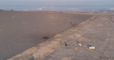Aerial view of a field with a crater and police vehicles investigating the scene.