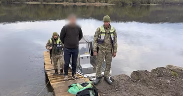 Ukrainian border guards standing on a wooden pier by a boat on the Dniester river.