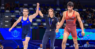 A Moldovan wrestler in a blue uniform being declared the winner by a referee.