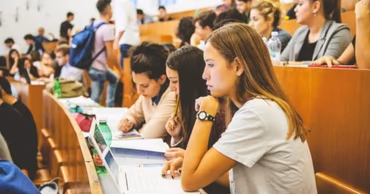 Students sitting in a university lecture hall using laptops and taking notes.