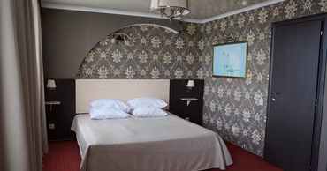A hotel room interior with a double bed, patterned wallpaper, and a swan painting.