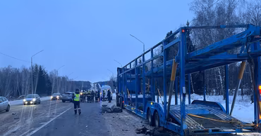 A large car carrier truck parked on the side of a snowy road with emergency responders.