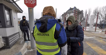 A border guard in a Moldova vest checking a person at a border crossing point.