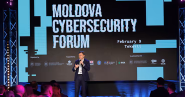 A speaker at the Moldova Cybersecurity Forum with the event logo and USAID branding visible.
