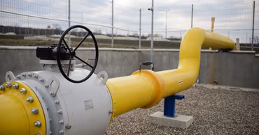 A yellow industrial gas pipeline with a valve in an outdoor setting.