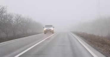 A white van driving on a road covered in dense fog.