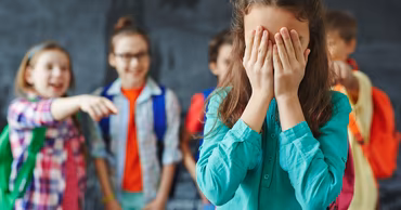 A young girl covering her face while other students point and laugh at her.