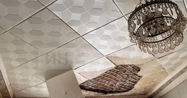 A damaged ceiling with a hole and hanging tiles in a residential apartment.