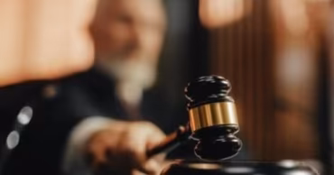 A judge's gavel striking a sounding block in a courtroom setting.