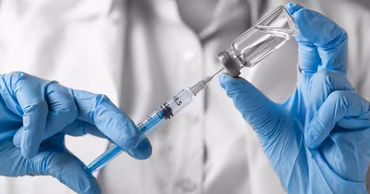 A medical professional in blue gloves preparing a vaccine injection from a glass vial.