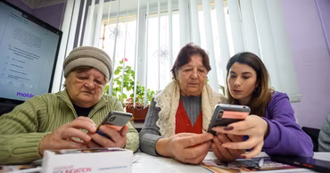 Two elderly women learning to use smartphones with the help of a younger person.
