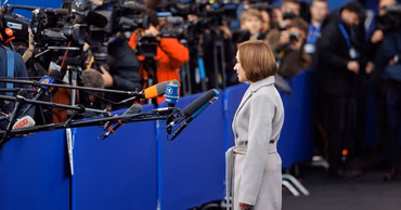 Maia Sandu standing in front of a group of journalists with microphones.