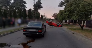 A red car overturned on the side of a road with another vehicle nearby.